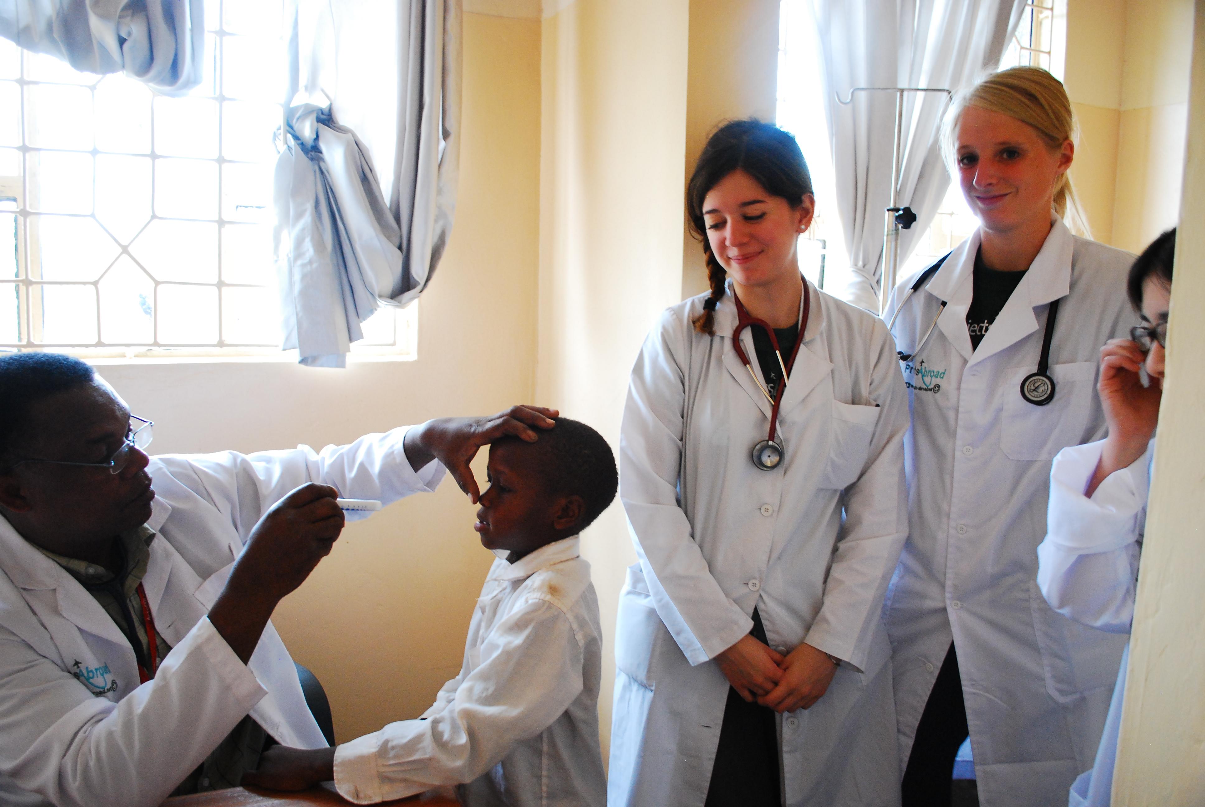 A doctor examines a young patient as students on the Public Health Internship for teenagers in Tanzania observe the consultation. During a Projects Abroad outreach in the local community, students on a Public Health placement for teenagers in Tanzania observe medical professionals.